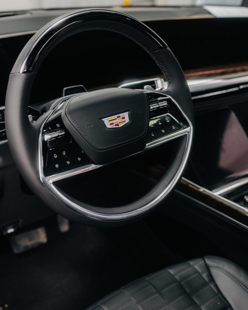 Close-up of a Cadillac interior showing the steering wheel with crest, digital dashboard, and premium leather seating.