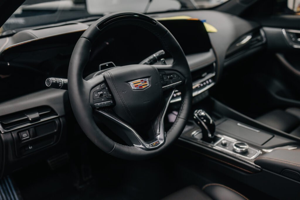 Interior view of a Cadillac vehicle showing the steering wheel with Cadillac crest, digital display, and center console controls.